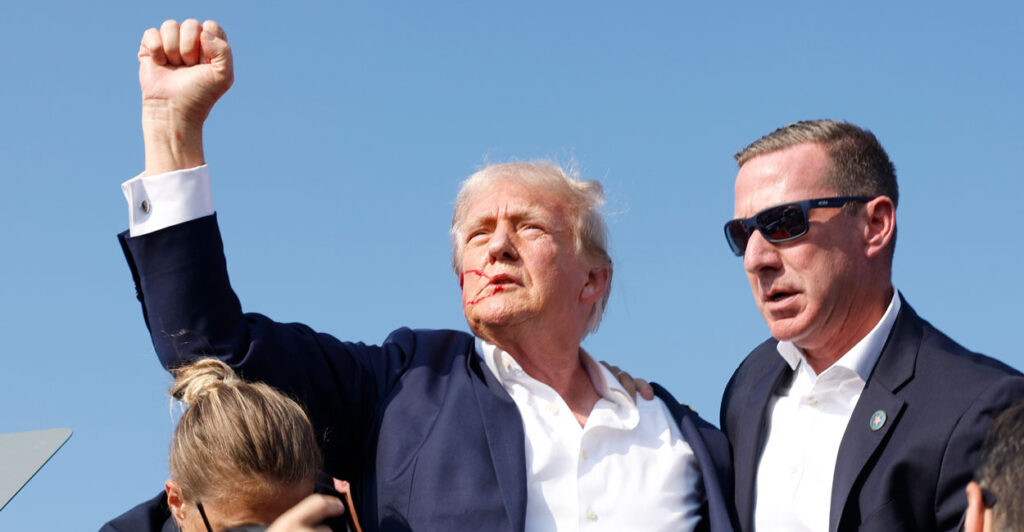 After being shot at by an assassin and with blood streaming down his face and his fist raised in the air, Donald Trump is rushed offstage by Secret Service during an outdoor rally
