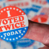 A finger holding an “I Voted Twice Today” sticker.