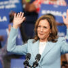 Kamala Harris wears a blue blazer and hold both hands up to a crowd.