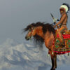 An American Indian sits on his Appaloosa horse on a high cliff in a desert area.