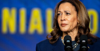 Kamala Harris Behind microphones in front of a blue background with yellow lettering