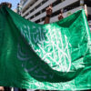 A group of people holding a Hamas flag and raising their arms.