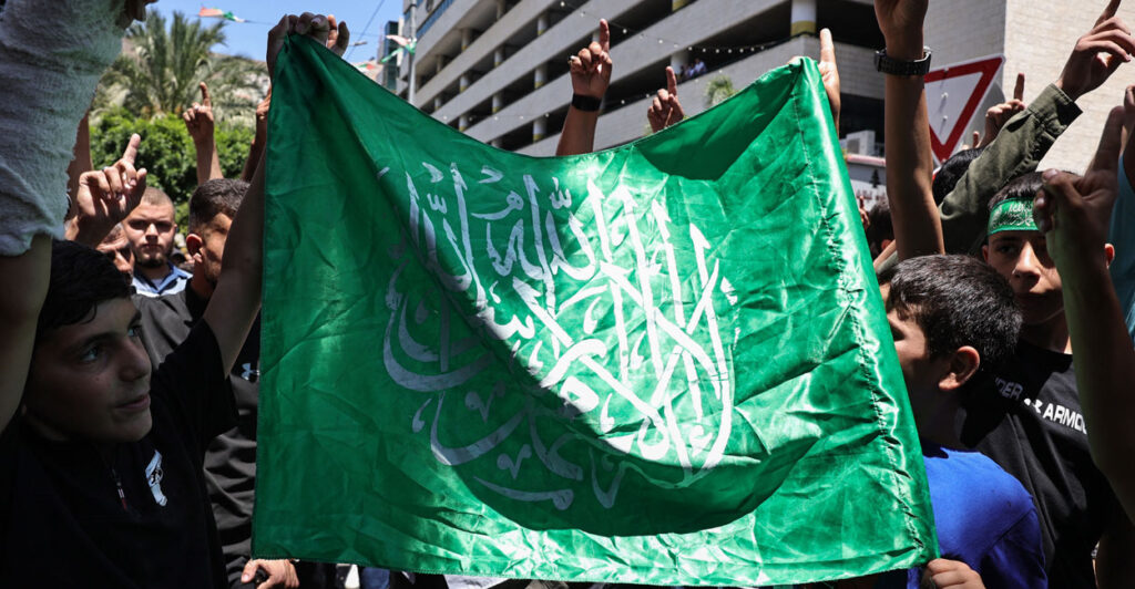 A group of people holding a Hamas flag and raising their arms.