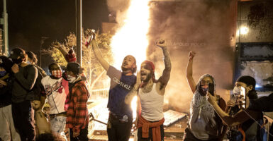 Rioters raise fists in front of the Minneapolis police station as it burns