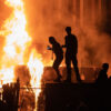 Rioters stand in front of a burning building