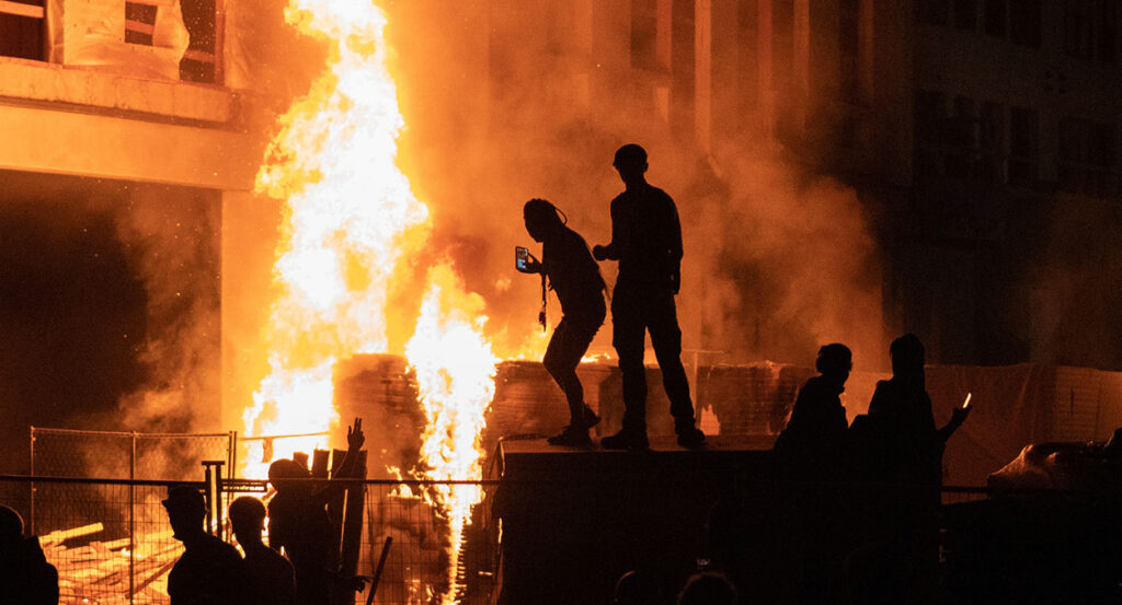 Rioters stand in front of a burning building