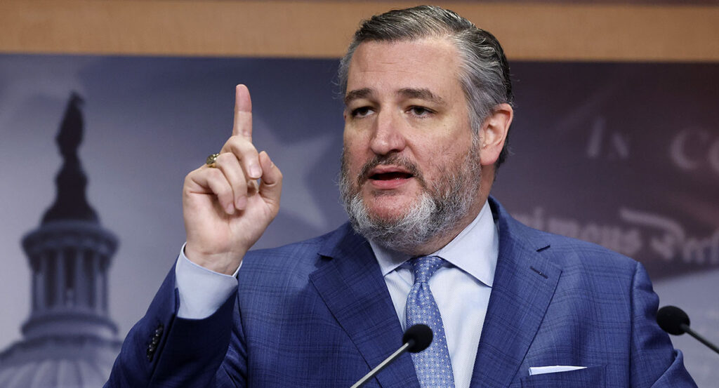 Ted Cruz, in a blue suit with a blue tie, raises his finger in front of a picture of the U.S. Capitol