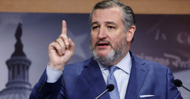 Ted Cruz, in a blue suit with a blue tie, raises his finger in front of a picture of the U.S. Capitol