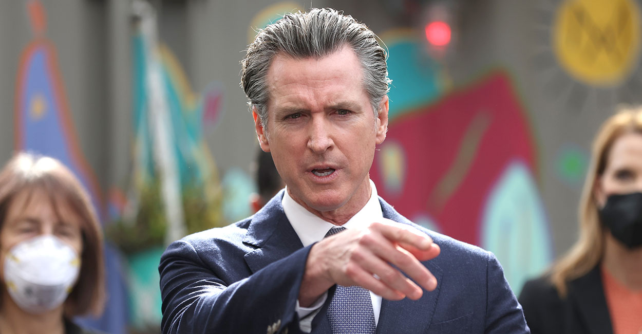 Gavin Newsom in a blue suit points in front of him
