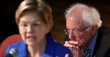 Elizabeth Warren in a blue blouse and Bernie Sanders in a blue suit