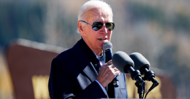 President Joe Biden holds a microphone and speaks in front of other microphones
